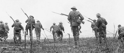 World War I soldiers wearing helmets and carrying rifles advance through a barbed wire field, moving forward in formation on a battlefield.