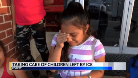 Young girl wipes her eyes while sitting outside a building. Text reads, “Taking care of children left by ICE.” Other children and an adult are partially visible nearby.